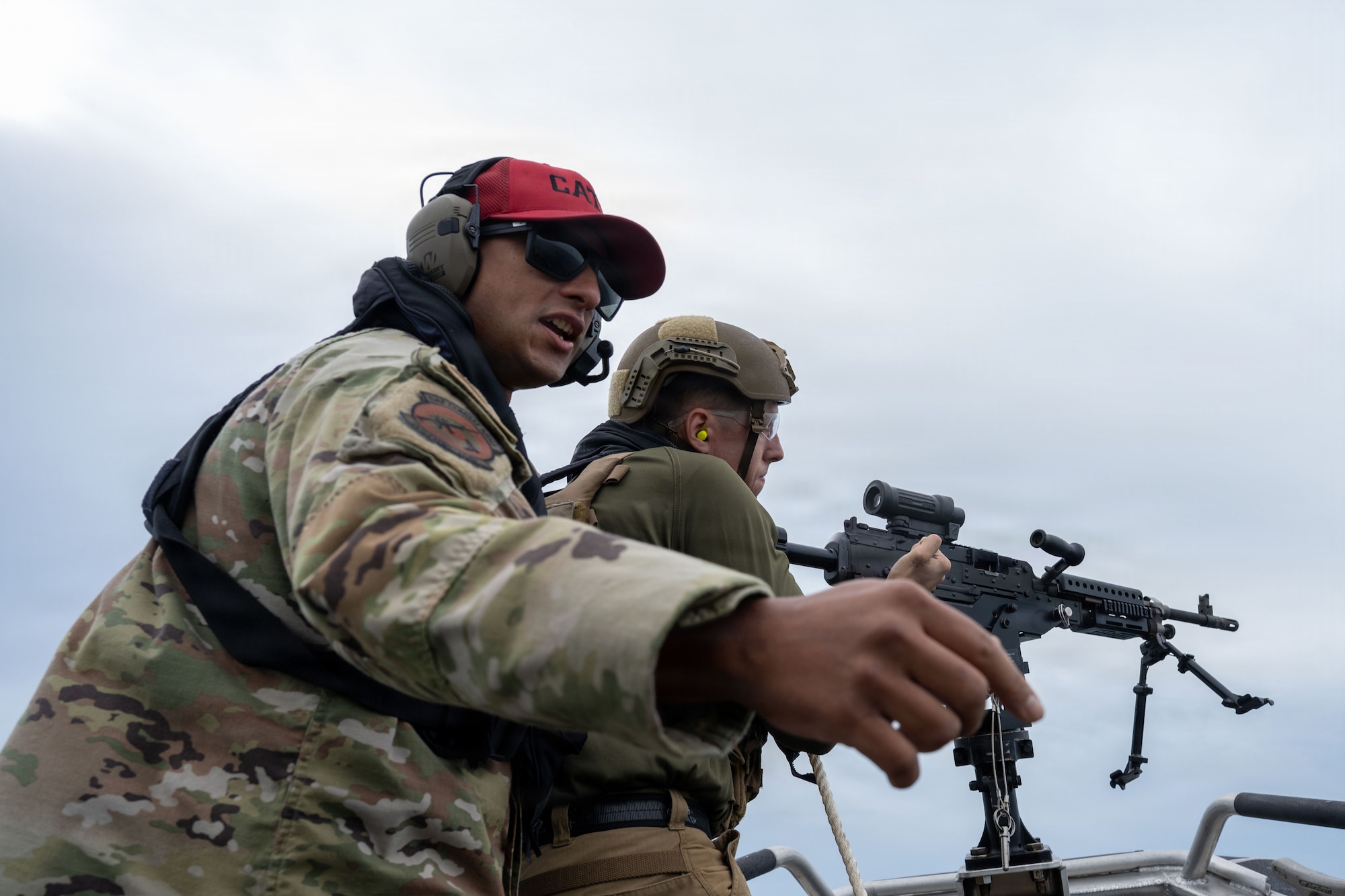 U.S. Air Force Tech. Sgt. Hunter Sterling, 6th Security Forces Squadron  combat arms training and maintenance (CATM) section chief, assists Senior Airman Travis Westrick,  6th SFS marine patrolman, while he fires a M240B machine gun off a vessel at MacDill Air Force Base, Florida, Nov. 6, 2025. Marine patrolmen are required to be certified in each weapon annually. CATM instructors ensure safety while helping improve a shooter's accuracy and confidence in the weapon. (U.S. Air Force photo by Airman Alexis Adams)