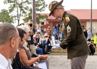 A soldier presents a ceremonial shell casing to the widow of Master Sgt. Gary Gordon who is sitting in the front row of the audience.