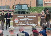A large entrance sign reading Welcome to Fort Gordon named in honor of Master Sgt. Gary I Gordon. United States Army, Cyber Center of Excellence. with a soldier and civilian on the left and a woman and soldier on the right.