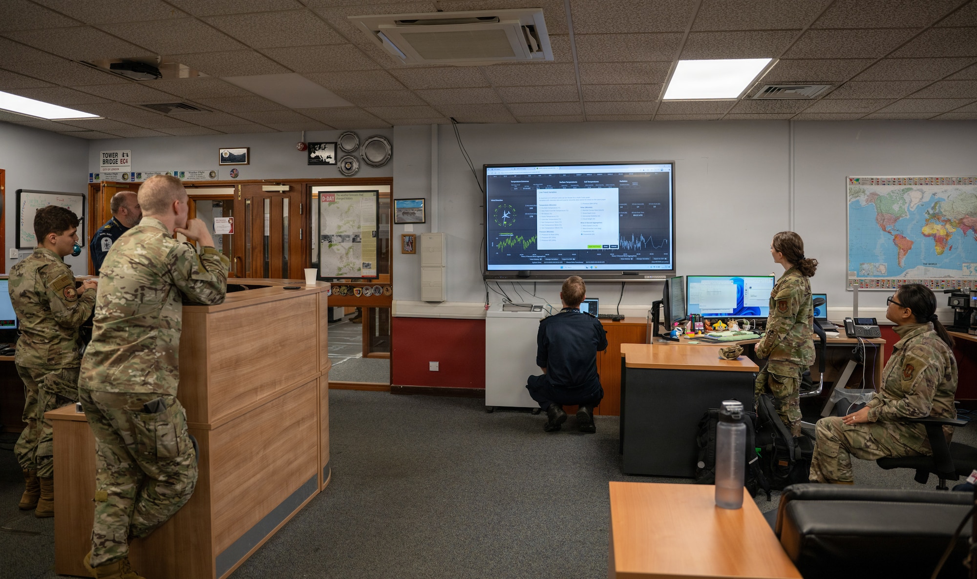 A group of military forecasters discuss what is displayed on a telvision screen.