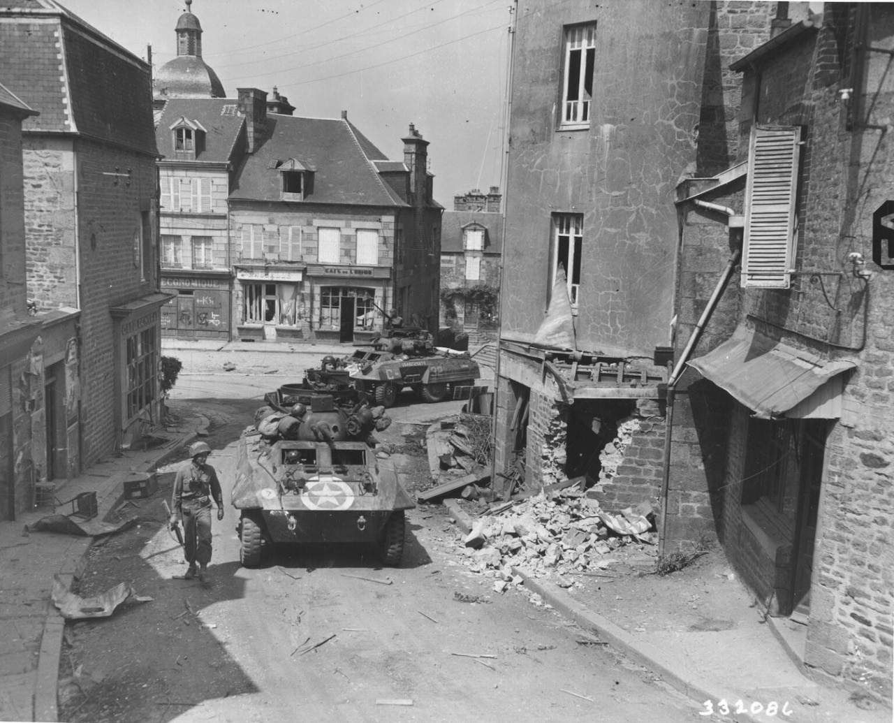 Two tanks move through small, winding streets in a dilapidated town.