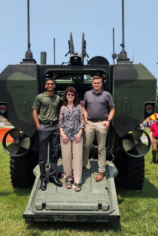 Three individuals pose for a photo on the ramp of an Amphibious Combat Vehicle.