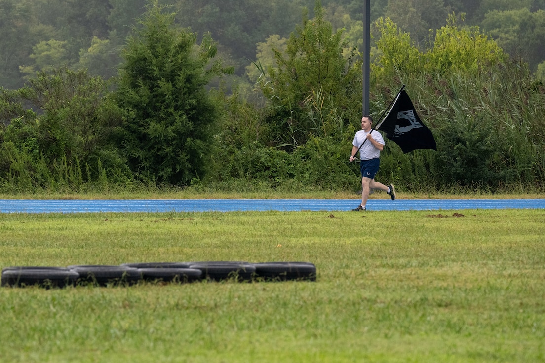 A man runs holding a black POW/MIA flag.