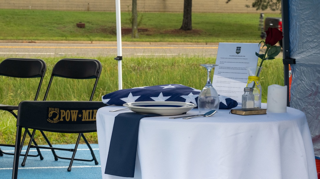 A table holding American flag, an overturned glass and a yellow ribbon.