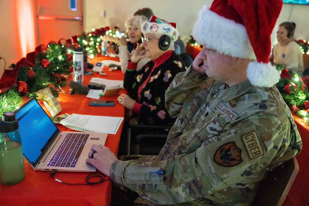 Three people wearing Santa hats answer phones at a red table decorated with lights and pine boughs.
