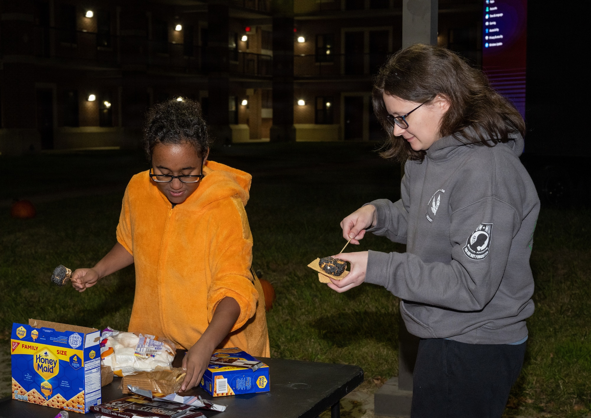 Two women make smores with roasted marshmallows.