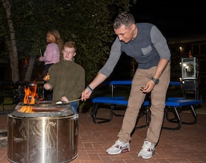 Two men hold marshmallows over a metal pit with fire.