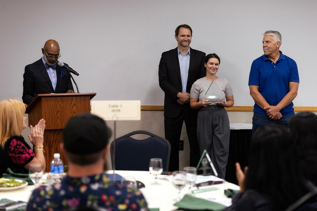 James Richardson, Keep Jacksonville Beautiful Commission member, commends Marine Corps Support Facility Blount Island’s success in implementing its Integrated Natural Resources Management Plan, which preserves critical ecosystems while supporting operational readiness, during the Environmental Achievement Awards luncheon Nov. 21, 2025, at the University of North Florida’s Adam W. Herbert University Center in Jacksonville, Florida. Clint Noble, Jacksonville Environmental Protection Board member, presented the Government and Institutional Achievement Award to Taylor Comstock, environmental protection specialist, and Shannon Easdale, environmental manager, both from Marine Corps Support Facility Blount Island. (Official Marine Corps photo by Dustin Senger)