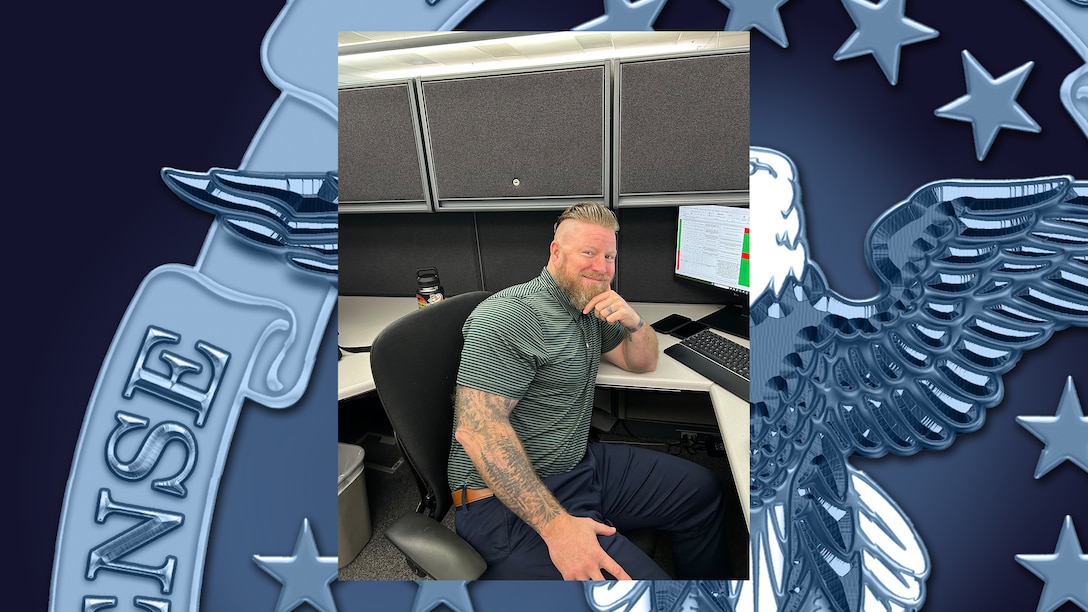 Man poses for photo at his desk.
