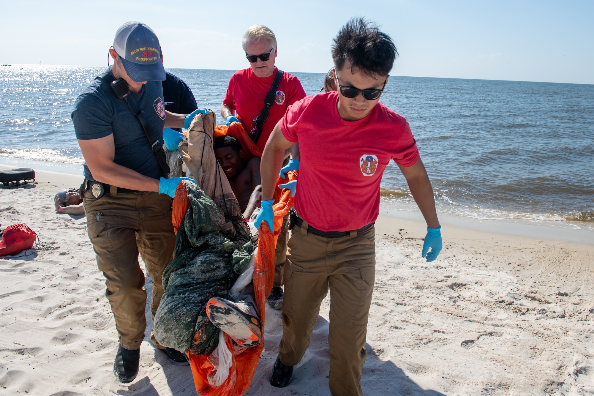 A group of people carry a person on a blanket in sand
