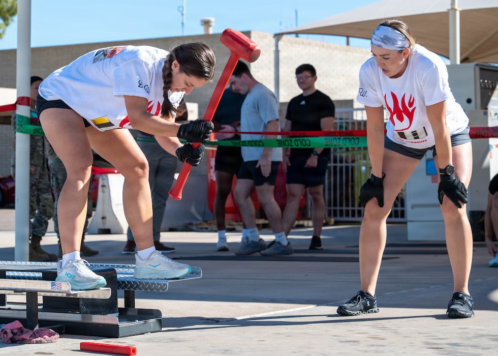 U.S. Air Force 1st Lt. Victoria Powe, 56th Civil Engineer Squadron engineering flight deputy, and Capt. Carly Wills, 56th CES Explosive Ordnance Disposal flight commander, power through the forcible-entry simulator during a firefighter challenge, Oct. 7, 2025, at Luke Air Force Base, Arizona. The event tested teamwork, strength, and endurance as part of Fire Prevention Week activities. Participants tackled multiple firefighting-inspired obstacles to promote safety and awareness.