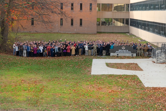 A large group of people stands outside behind the Nuclear Command, Control and Communications Integration Directorate sign