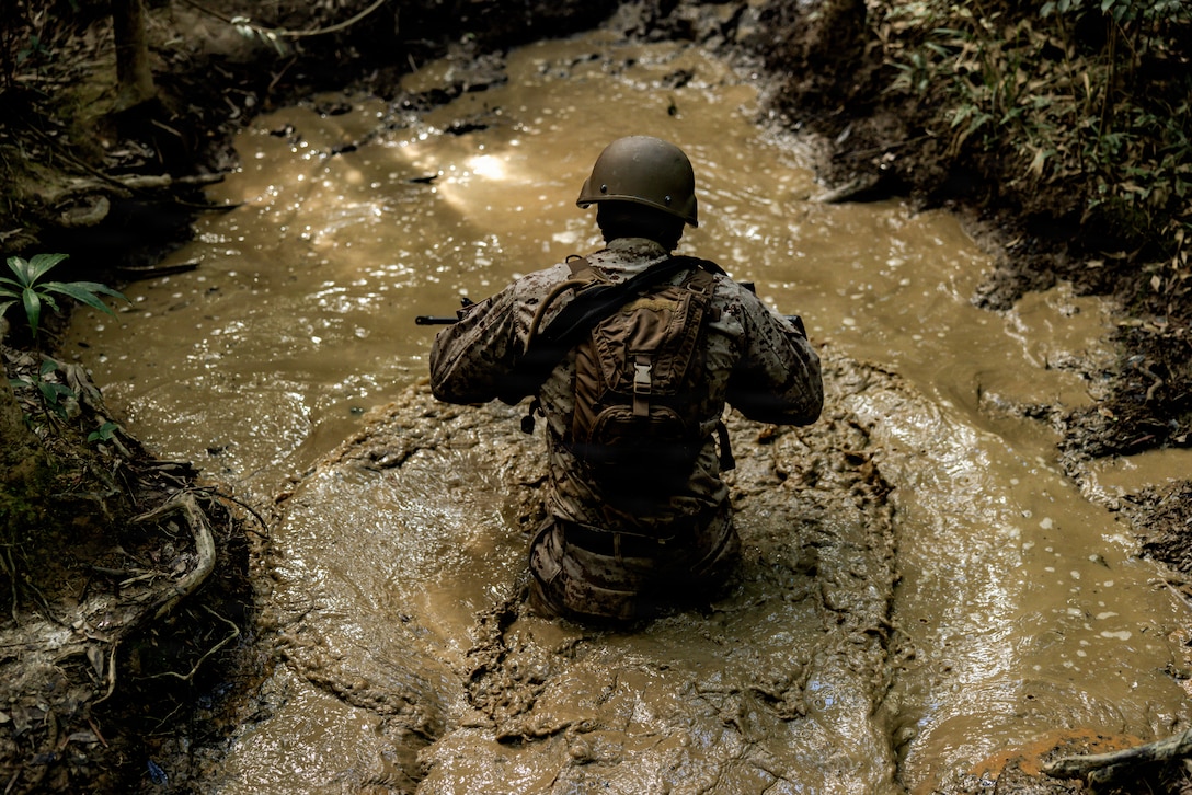 U.S. Marine Corps Lance Cpl. Jeremy BonillaEspinoza, a native of New York and a satellite communications operator maintainer with 7th Communication Battalion, III Marine Expeditionary Force Information Group, maneuvers through a muddy creak during Operation Odyssey Stormbreaker III at Jungle Warfare Training Center, Okinawa, Japan, Nov. 4, 2025.