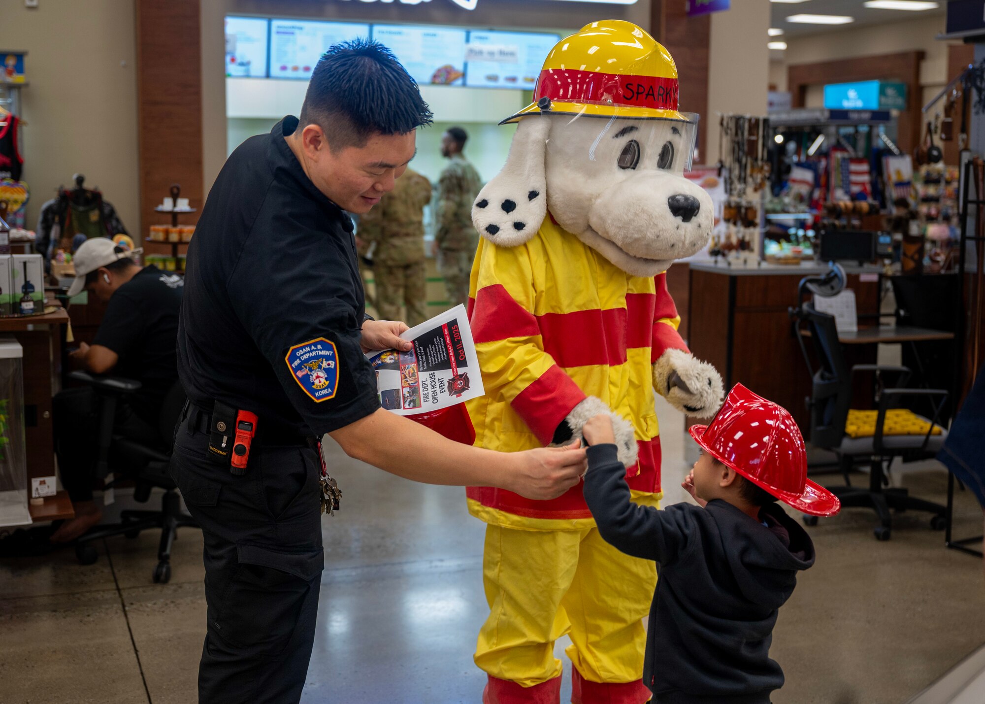 Lee Ji Ho, 51st Civil Engineer Squadron fire inspector, and Sparky the Fire Dog hand out a fire badge during Fire Prevention Week at Osan Air Base, Republic of Korea, Oct. 7, 2025. This year’s Fire Prevention Week theme was “Charge into Fire Safety: Lithium-ion Batteries in Your Home”, serving as a reminder that fires can start from something as small as a battery. (U.S. Air Force photos by Staff Sgt. Sarah Williams)