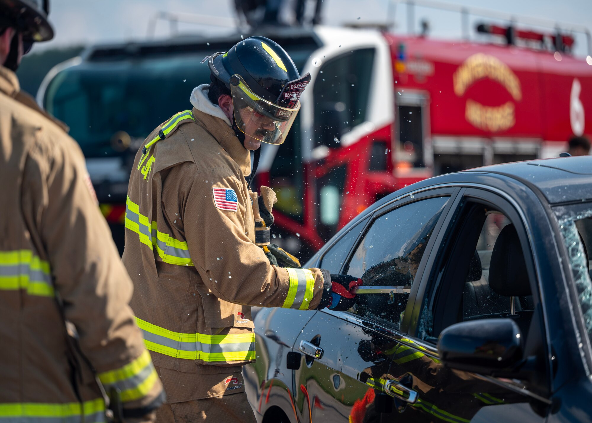 U.S. Air Force Senior Airman Aidan Lohr, 51st Civil Engineer Squadron firefighter, shatters a car window at an open house event during Fire Prevention Week at Osan Air Base, Republic of Korea, Oct. 11, 2025. Breaking windows allows firefighters to reach victims quickly and safely. (U.S. Air Force photos by Staff Sgt. Sarah Williams)