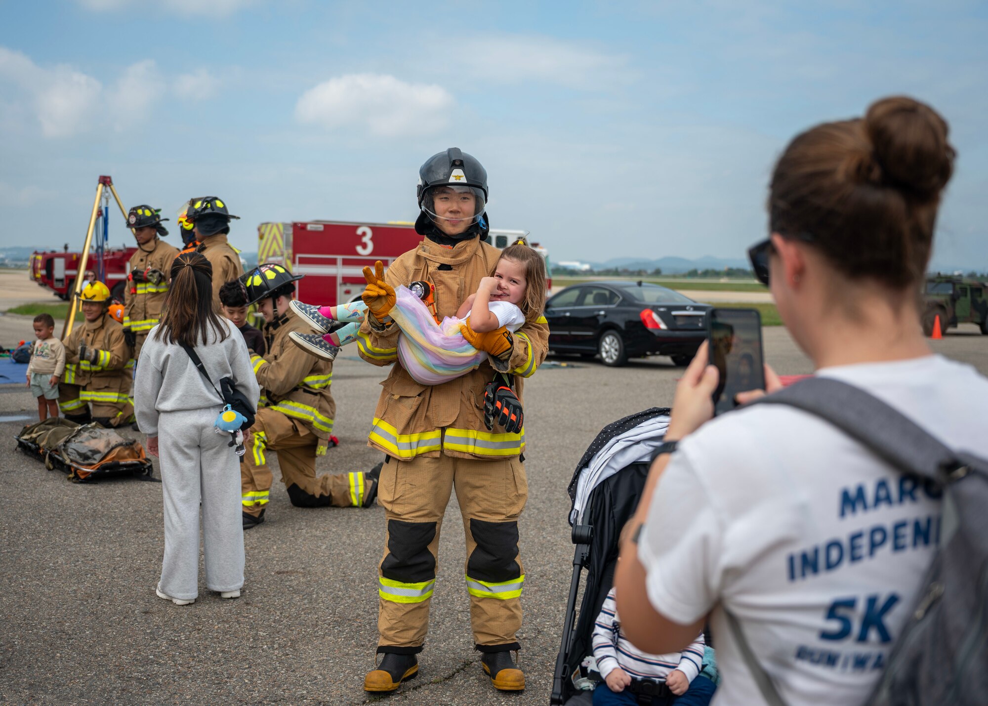 Republic of Korea Air Force Staff Sgt. Bae Sangbin, ROKAF firefighter, holds an open house participant during Fire Prevention Week at Osan Air Base, Republic of Korea, Oct. 11, 2025. Fire Prevention Week is observed each year during the week of Oct. 9 in commemoration of the Great Chicago Fire of 1871.  (U.S. Air Force photos by Staff Sgt. Sarah Williams)