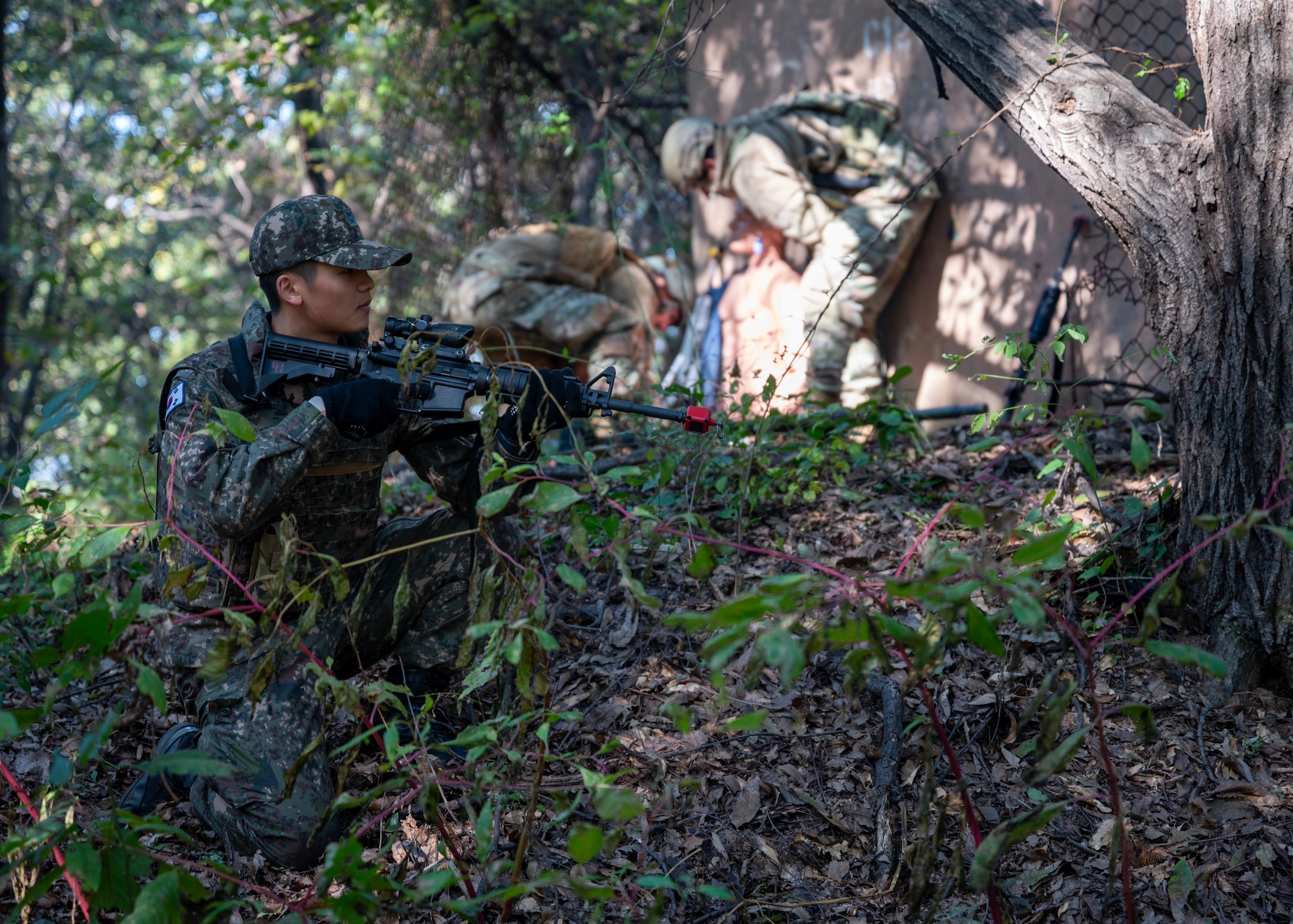 Republic of Korea Air Force Tech. Sgt. Hong Min Hyuk, military police, stands guard while 51st Security Forces members extract a simulated body during a Combat Readiness Course at Osan Air Base, Republic of Korea, Oct. 29, 2025. The involvement of ROKAF added a critical joint-training experience, ensuring both forces can respond seamlessly during real-world contingencies. (U.S. Air Force photo by Staff Sgt. Sarah Williams)