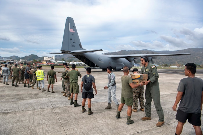 U.S. Air Force Airmen, U.S. Marines and the Armed Forces of the Philippines servicemembers distribute family food packs in a line during a foreign disaster relief operation.