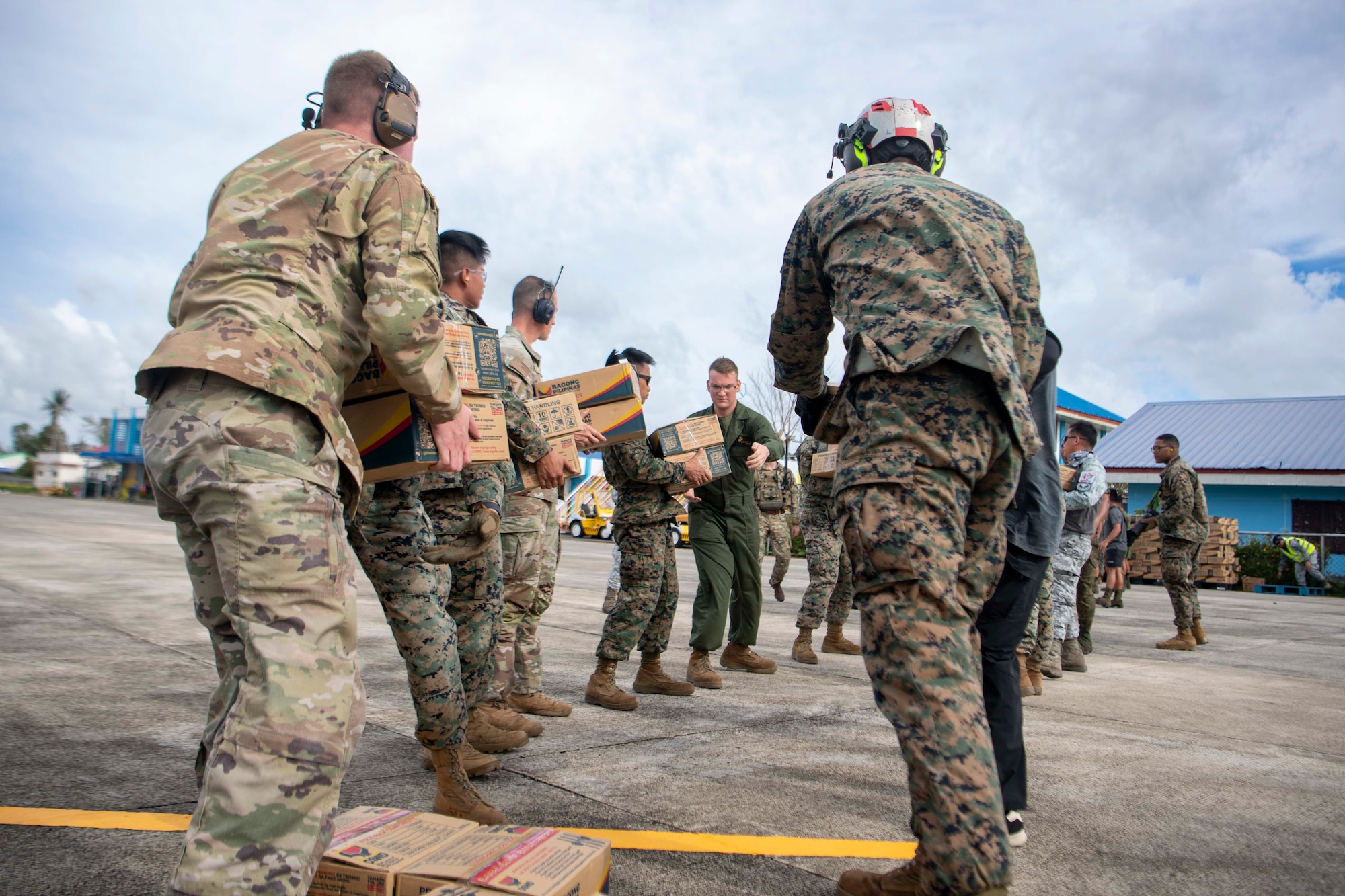 U.S. Air Force Airmen, U.S. Marines and Armed Forces of the Philippines service members distribute family food packs in a line during a foreign disaster relief operation.