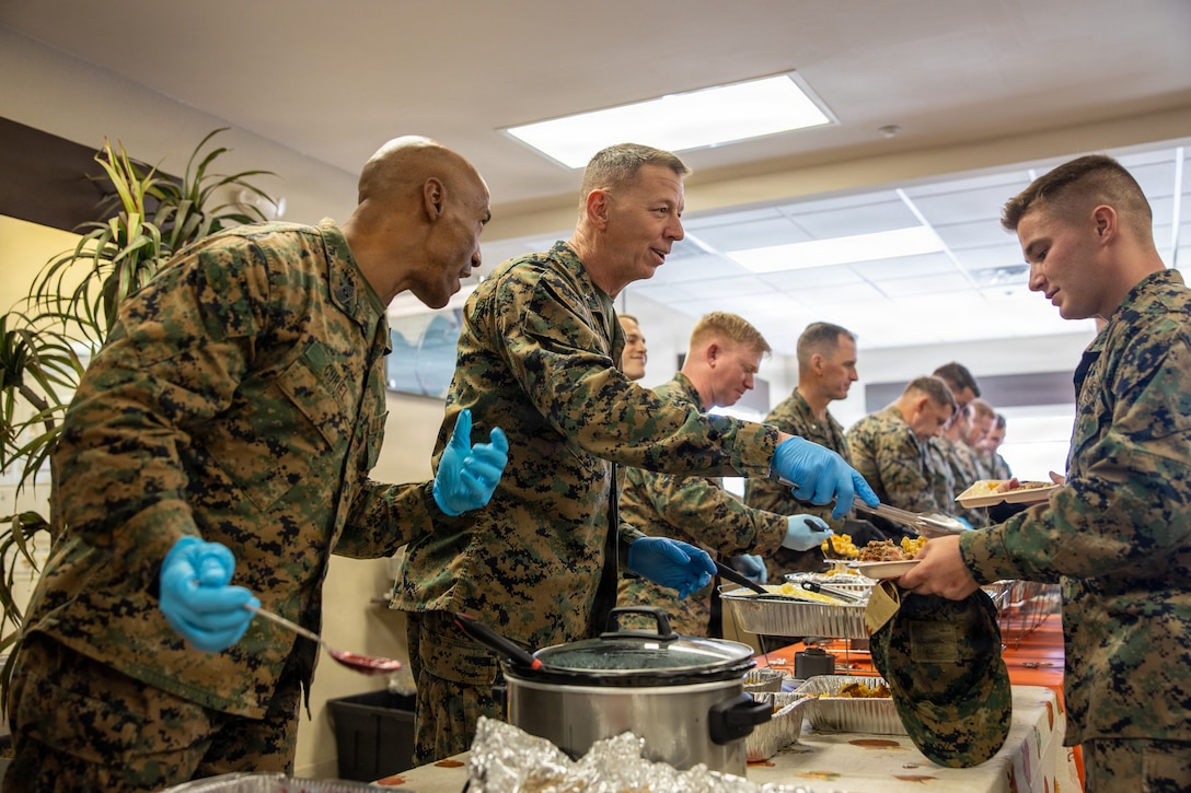 U.S. Marine Corps Sgt. Maj. Crispiniano D Curiel, left, the senior enlisted advisor of II Marine Expeditionary Force Support Battalion and a native of Perth Amboy, New Jersey, and Brig. Gen. Joel Schmidt, center, the assistant division commander of 2nd Marine Division and a native of Robinson, Illinois, serve food to Marines and Sailors with II MEF during a Thanksgiving potluck at Marine Corps Base Camp Lejeune, North Carolina, Nov. 20, 2025. II MEF hosted the Thanksgiving potluck to bring Marines and Sailors together to build camaraderie and unit cohesion while celebrating the holiday season. (U.S. Marine Corps photo by Lance Cpl. Dorian Melrath)