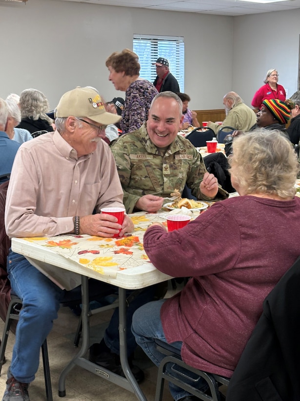Man in military uniform sits at table with older couple smiling/talking