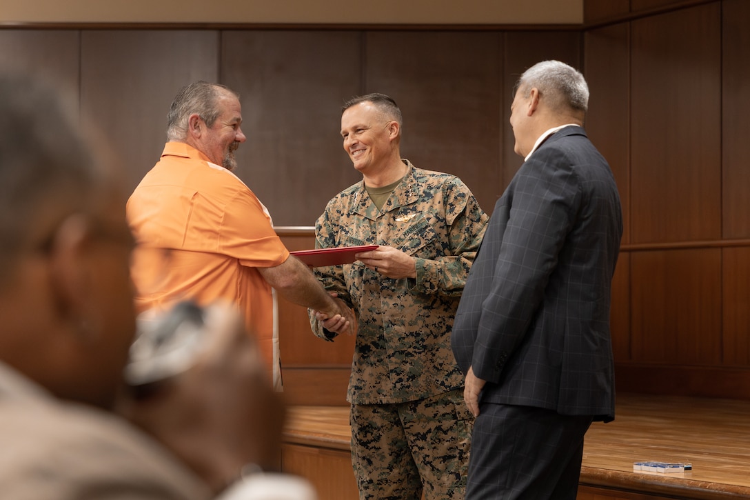 U.S. Marine Corps Lt. Gen. Leonard F. Anderson IV, center, commander of Marine Forces Reserve and Marine Forces South, and Gregg T. Habel, right, executive director of Marine Forces Reserve and Marine Forces South, awards Cliff Myers, a capabilities analyst with Marine Forces Reserve, during a town hall meeting at the Marine Corps Support Facility New Orleans, Nov. 20, 2025. Myers was awarded Mid-Grade Civilian of the Quarter during the town hall meeting. (U.S. Marine Corps photo by Lance Cpl. Carlina Holland)