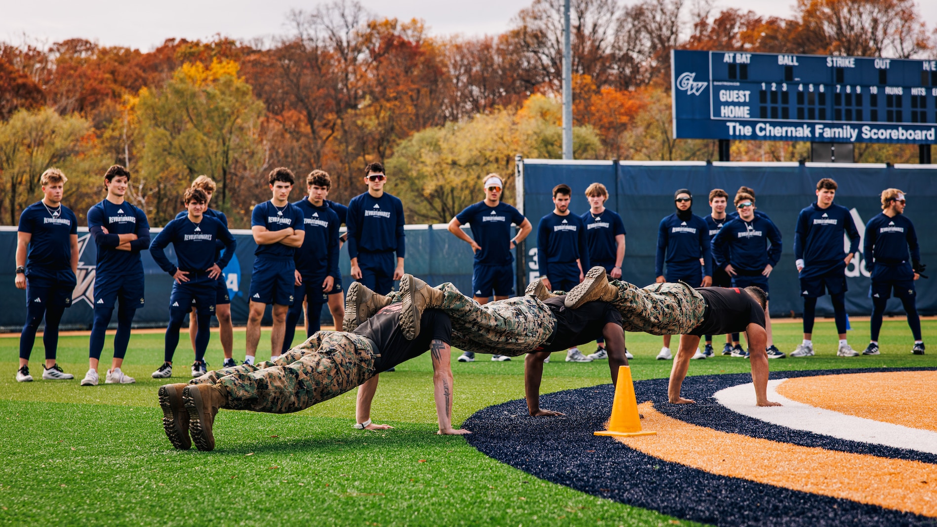 U.S. Marine Corps Gunnery Sgt. Jack Pavao, Staff Sgt. John Lewis, and Sgt. Ar’kel Brown, all Martial Arts Instructor Trainer with the Martial Arts and Fitness Center of Excellence, demonstrate squad push-ups to baseball players with George Washington University during a physical training event at Tucker Field in Arlington, Virginia, Nov. 14, 2025. Marines with the MAFCE challenged the GWU baseball team in a physical training event to inspire and train in team building skills in order to develop a greater sense of unit leadership, further uniting the team. (U.S. Marine Corps photo by Cpl. Braydon Rogers)