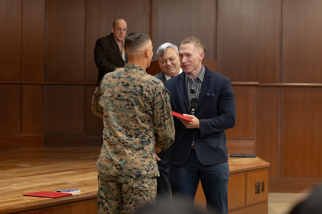 Martin E. Morgan, right, communications directorate with Marine Forces South receives an award from U.S. Marine Corps Lt. Gen. Leonard F. Anderson IV, commander of Marine Forces Reserve and Marine Forces South, during a town hall meeting at Marine Corps Support Facility New Orleans, Nov. 20, 2025. Morgan was awarded for being the Mid-Grade Civilian of the Quarter. (U.S. Marine Corps photo by Lance Cpl. Van Hoang)