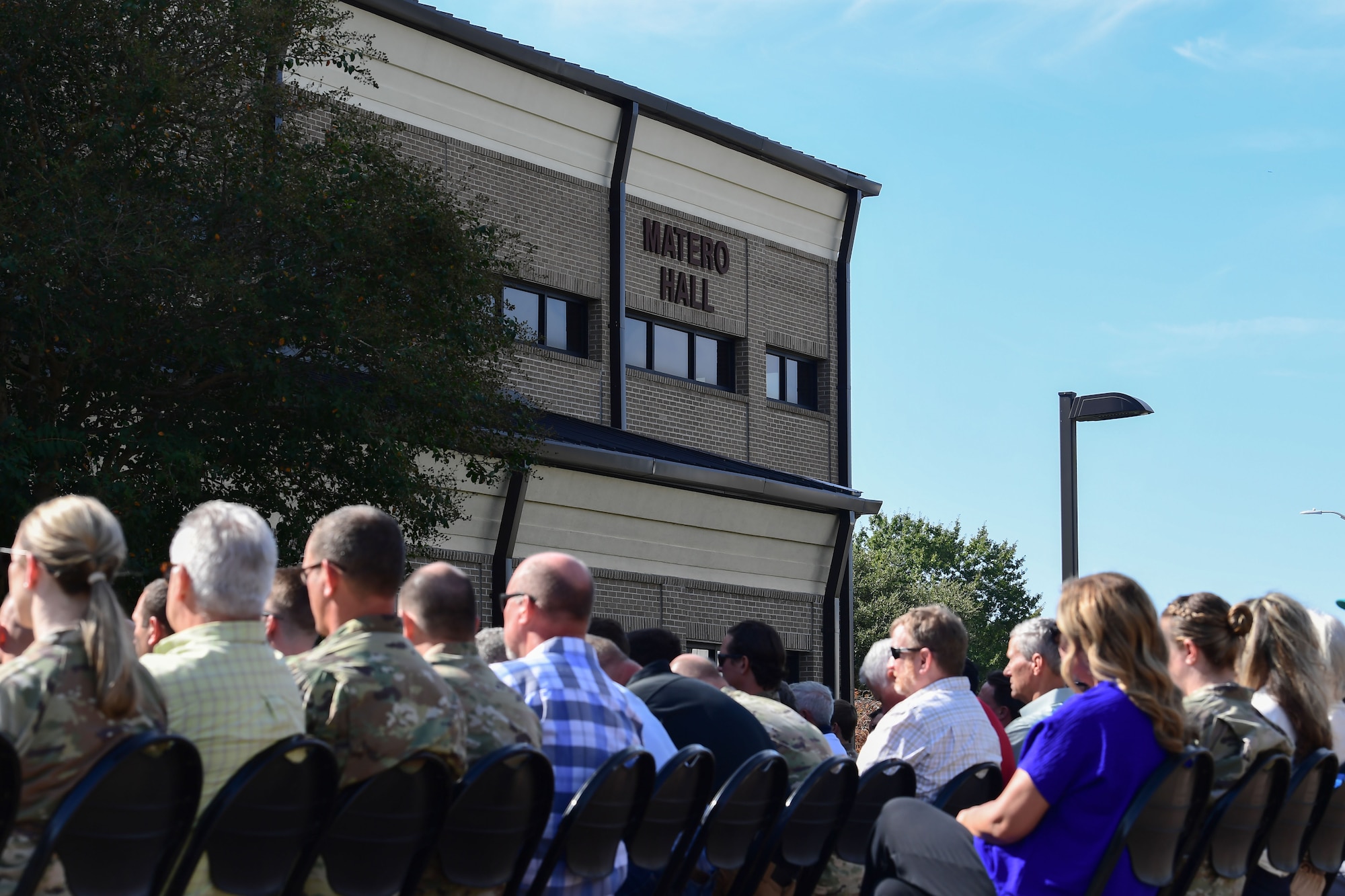 A group of people sit in a crowd facing a buidling
