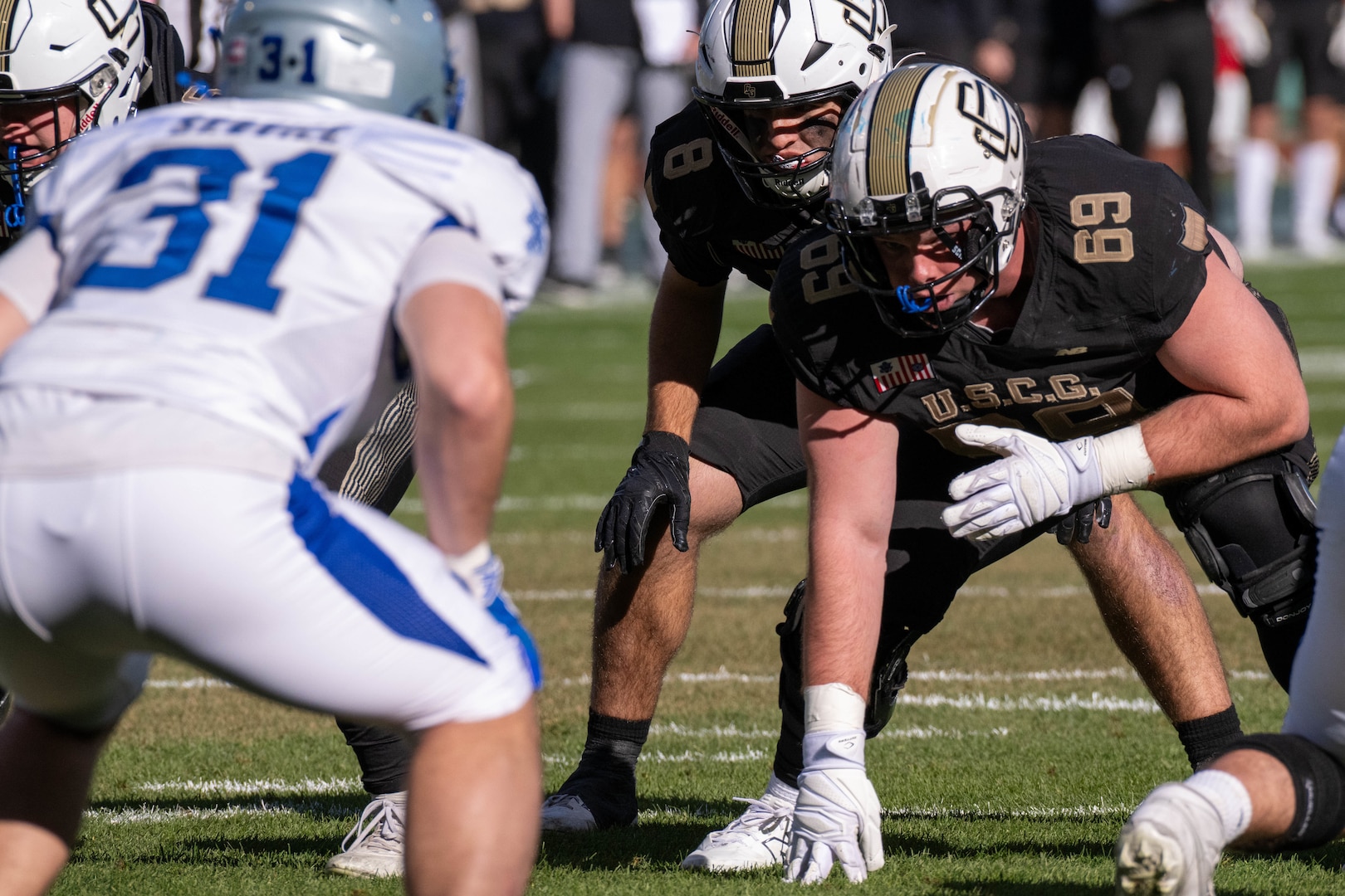 U.S. Coast Guard Academy football players face U.S. Merchant Marine Academy football players on the defensive line during the 54th Secretaries’ Cup at Fenway Park, Boston, Nov. 15, 2025. In 2003, “Secretary’s Cup” was pluralized when the U.S. Coast Guard moved to the Department of Homeland Security. (U.S. Coast Guard photo by Petty Officer Third Class Leo Avila.)