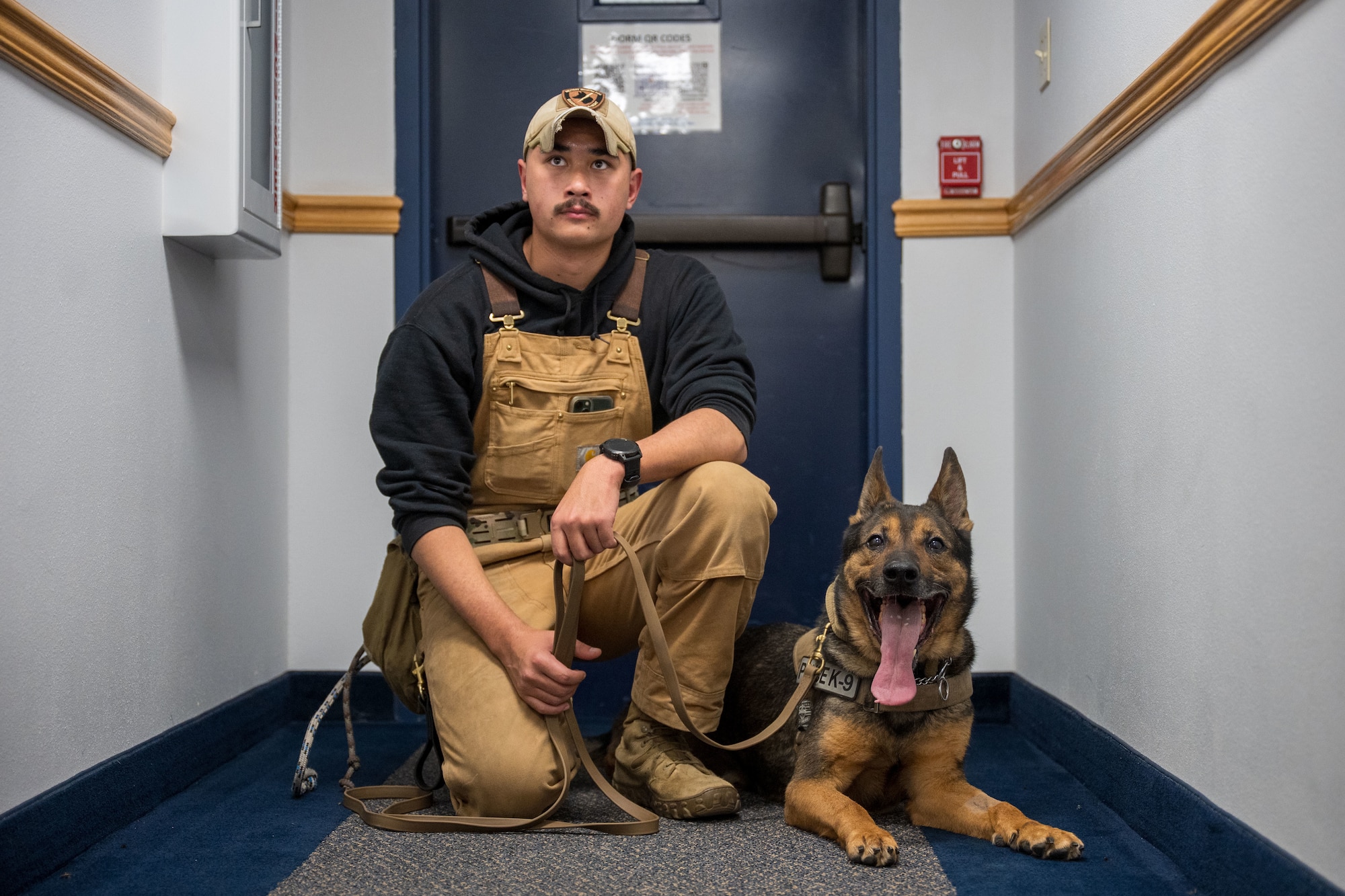A man is crouched while a dog next to him is laying down.