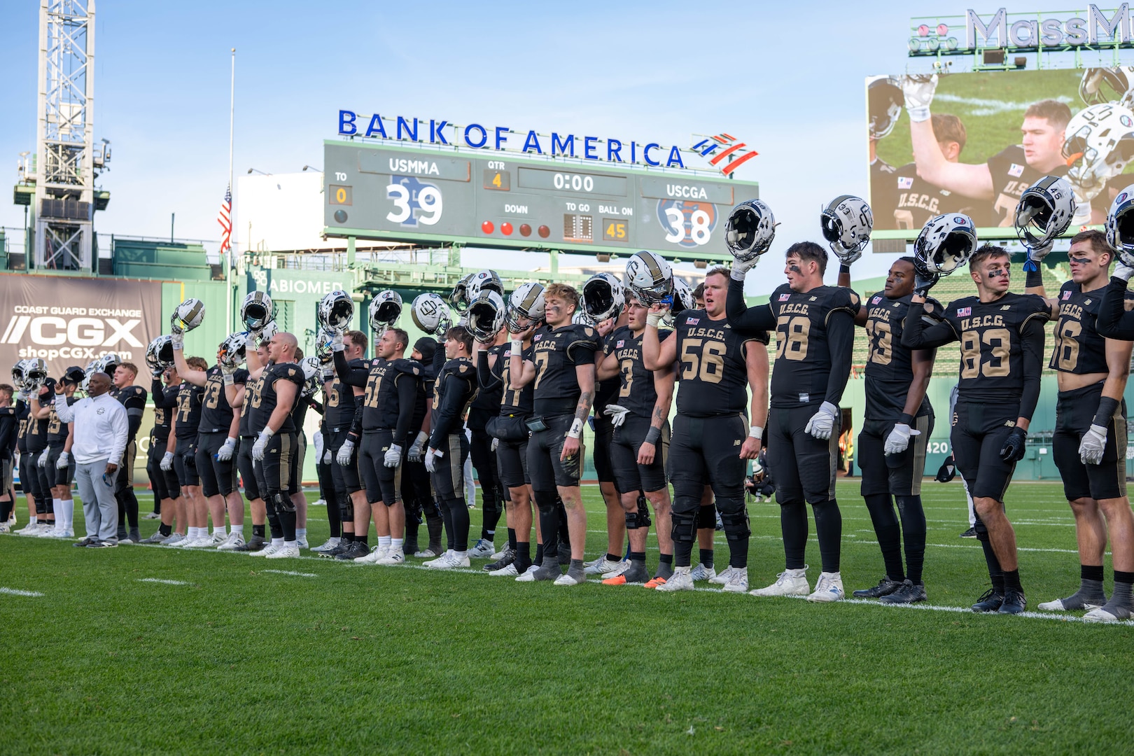 U.S. Coast Guard Academy (USCGA) football team raise their helmets while the USCGA alma mater played, standing on the field during the 54th Secretaries’ Cup at Fenway Park, Boston, Nov. 15, 2025. This is the first time USCGA and the U.S. Merchant Marine Academy have played outside of their home fields for a Secretaries’ Cup game. (U.S. Coast Guard photo by Petty Officer Second Class Janessa Warschkow.)