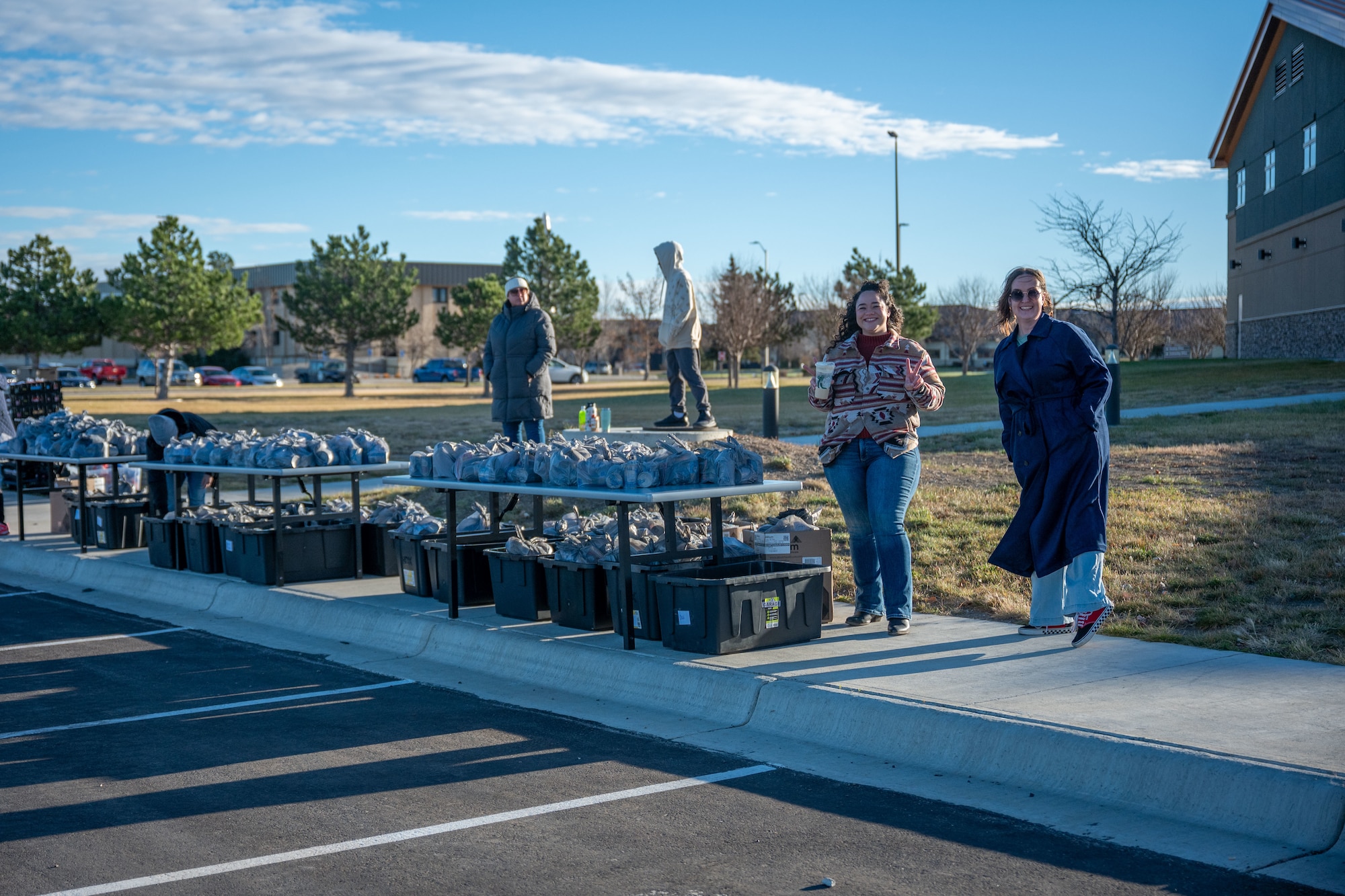A group of people standing around tables with bags of food on top.