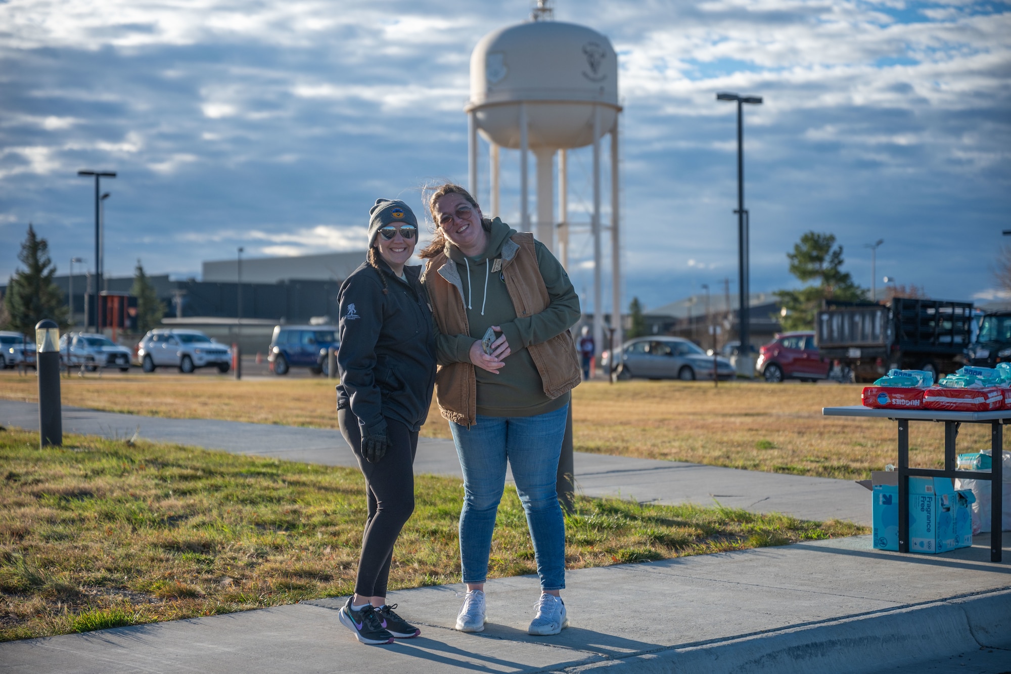 Two women posing for a photo outside with a water tower in the background.