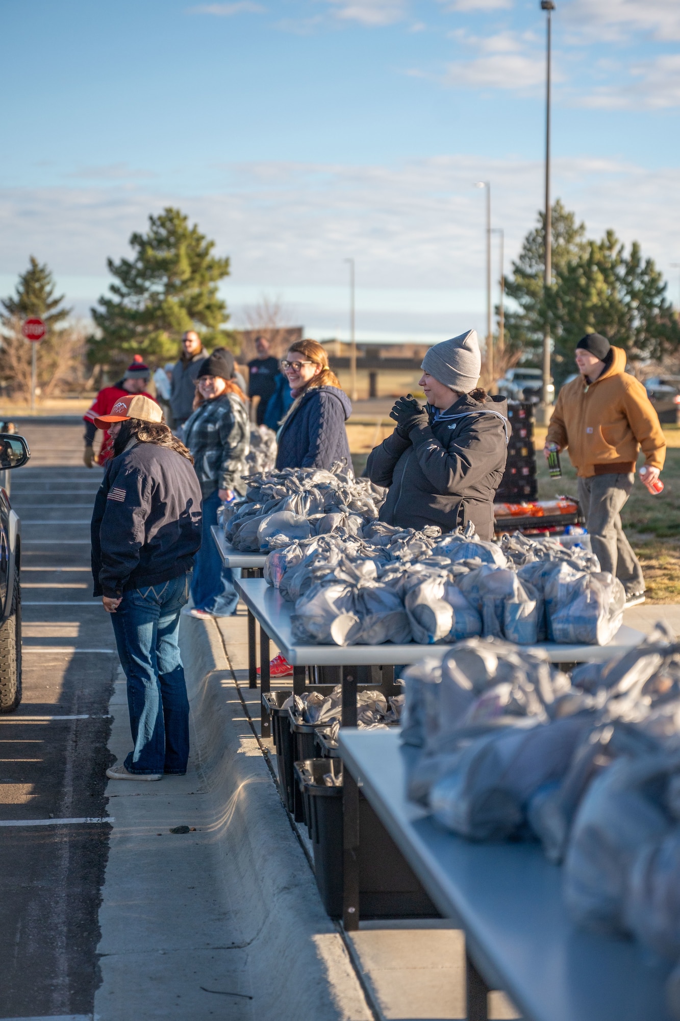 A group of people standing around tables with bags of food on top.