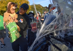A man holds his son who is wearing a costume while trunk or treating