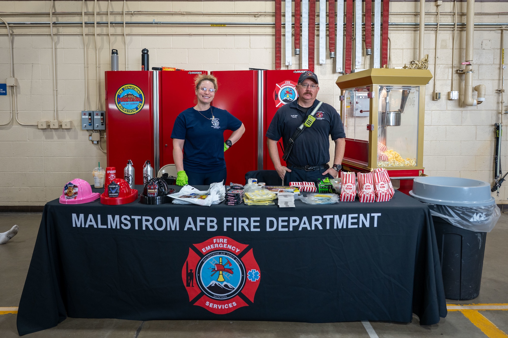Two firefighters posing for a picture behind a table.