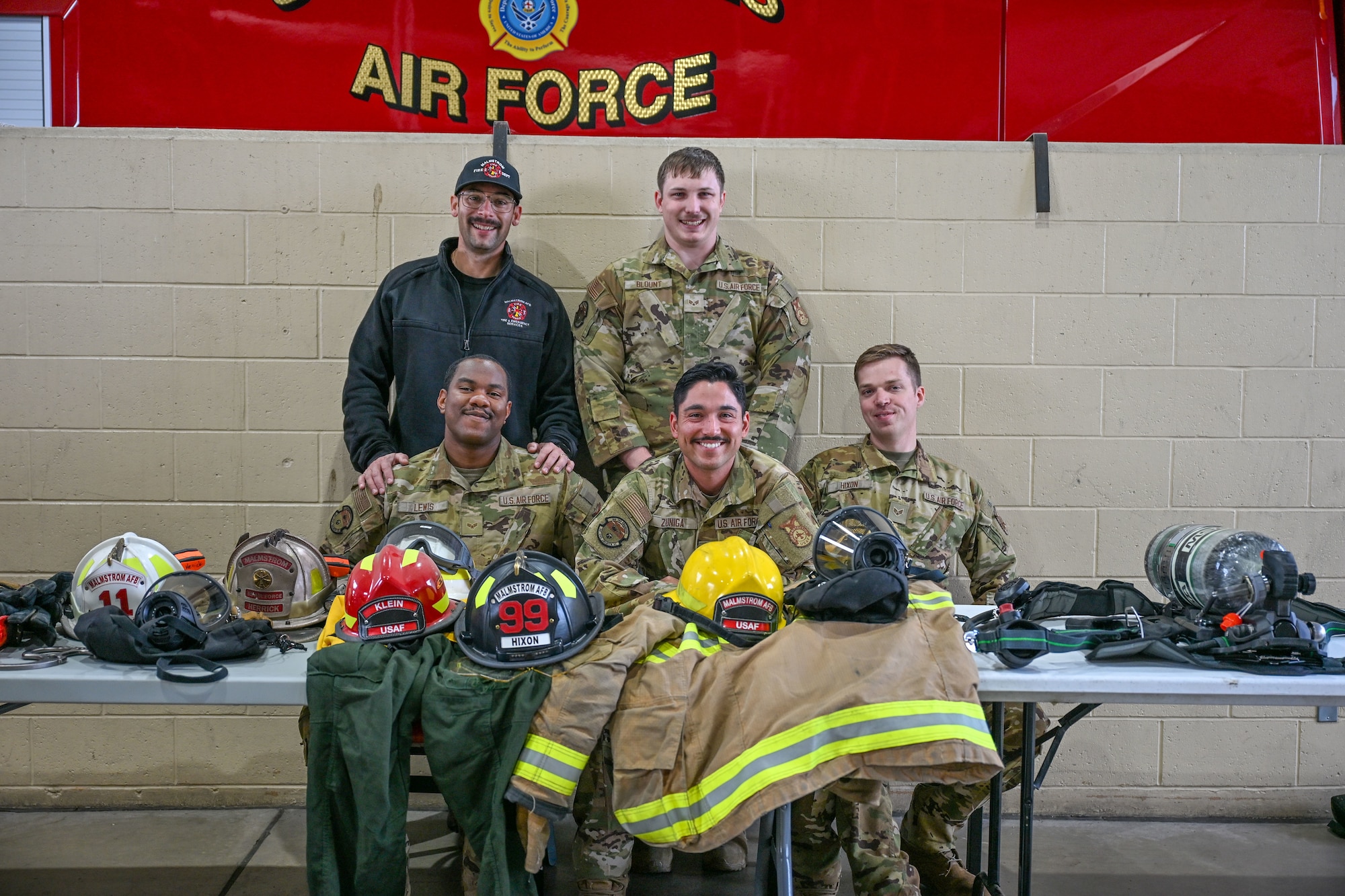 Five Airmen posing for a picture behind their firefighter gear.