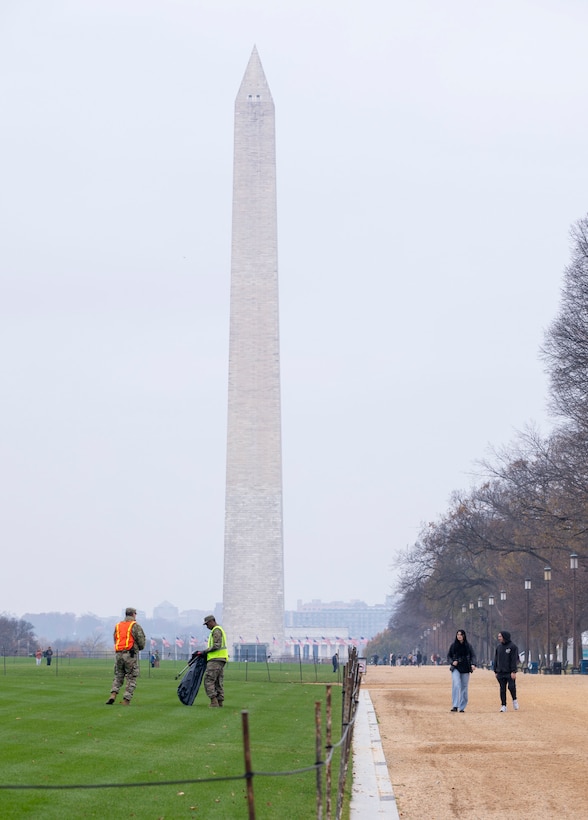 Two guardsmen in reflective vests collect trash in front of a monument on a foggy day.