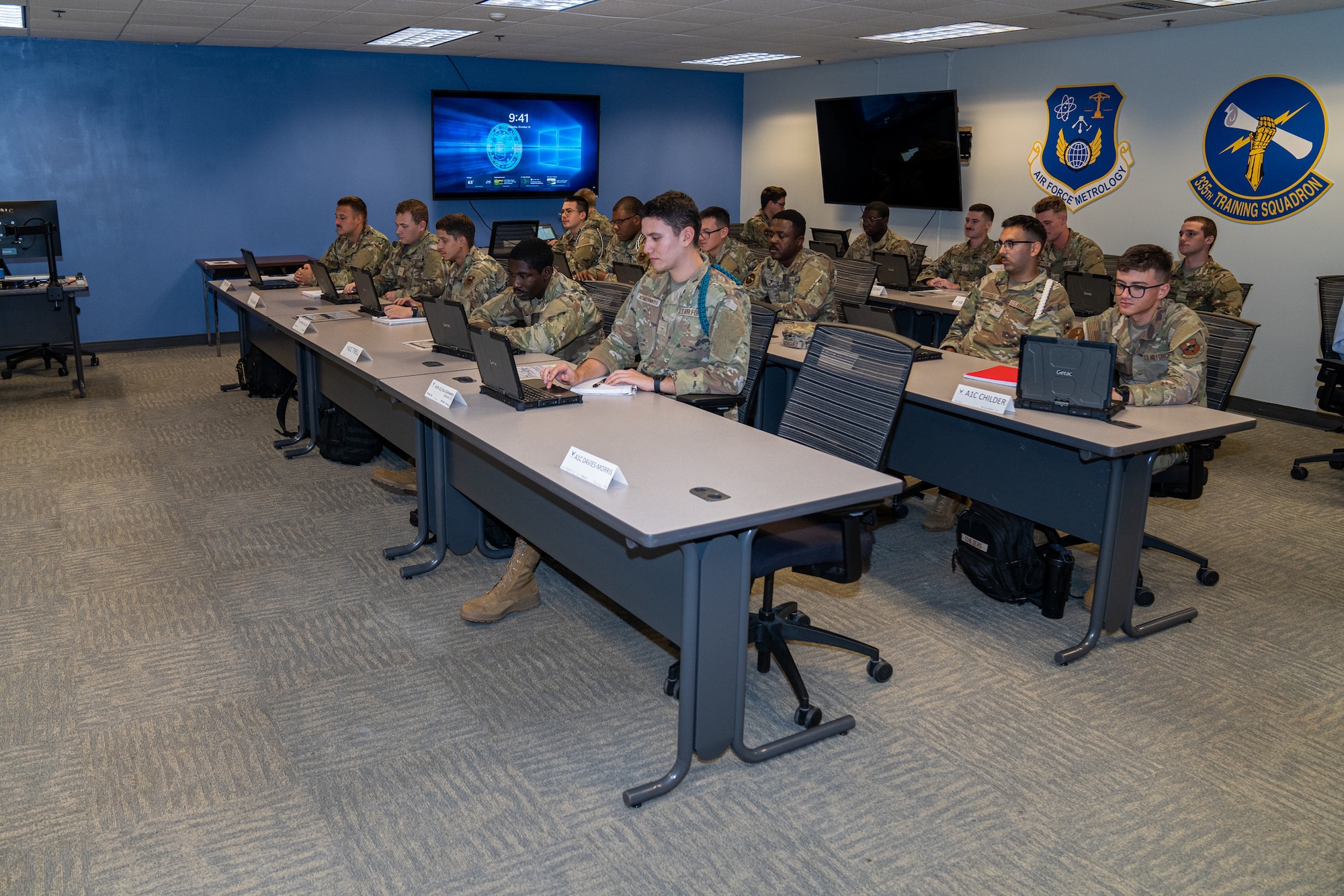 Service members in OCPs sit in a classroom.