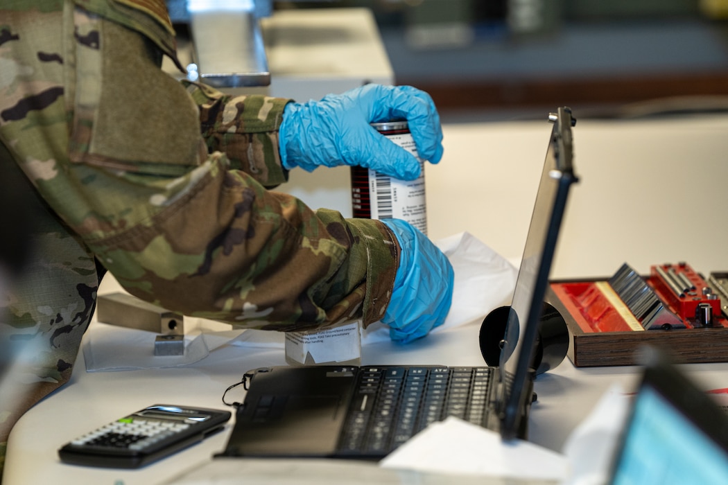 A serviceman in OCPs wearing light blue latex gloves handles a can.