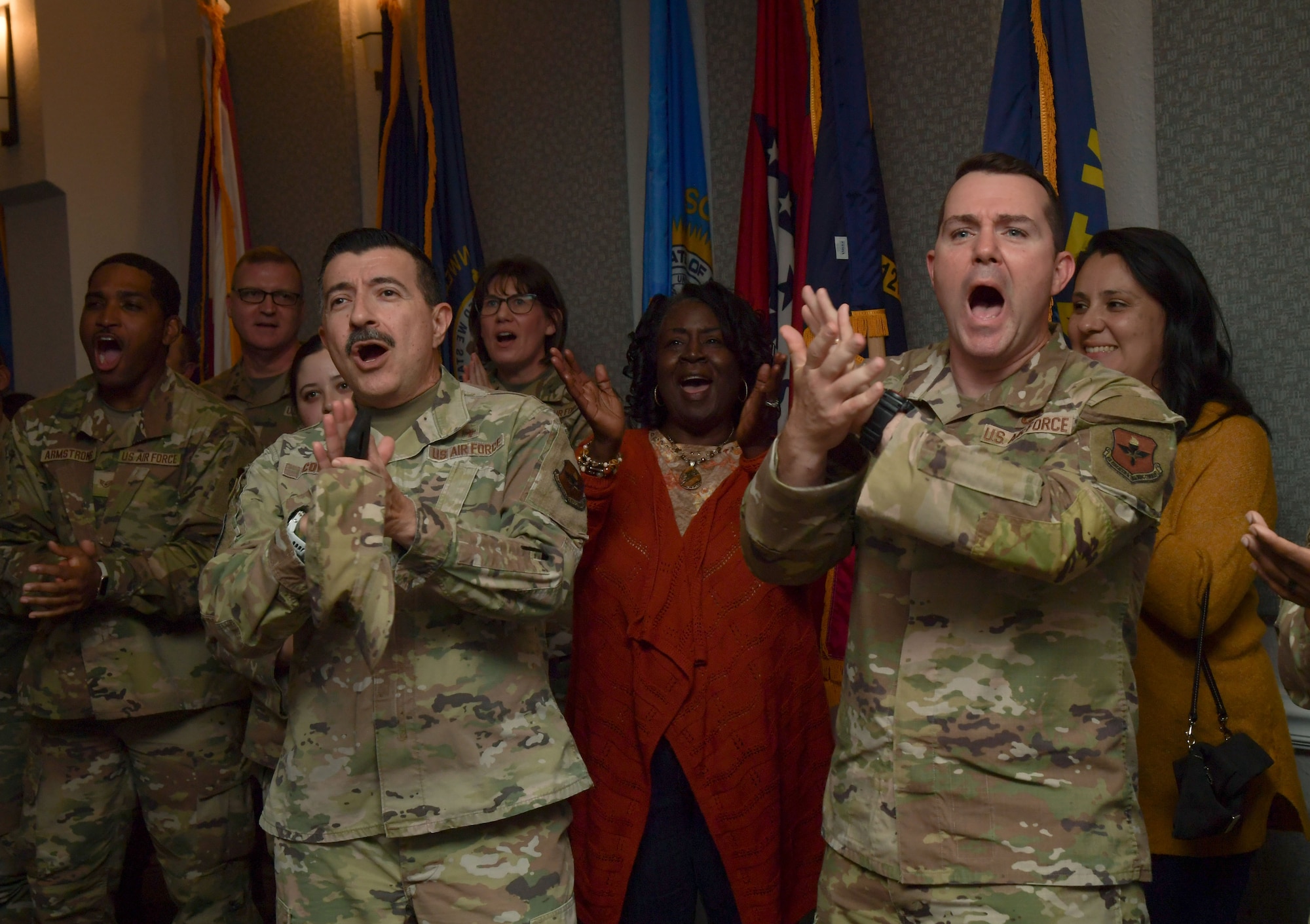 Two men wearing military uniforms clap in front of a group of people