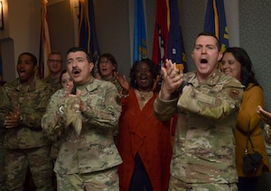Two men wearing military uniforms clap in front of a group of people