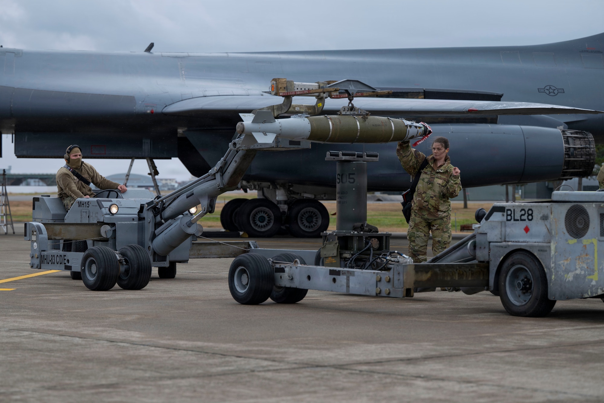Airmen prepare to load a large weapon onto a B-1 Lancer outside on the flightline