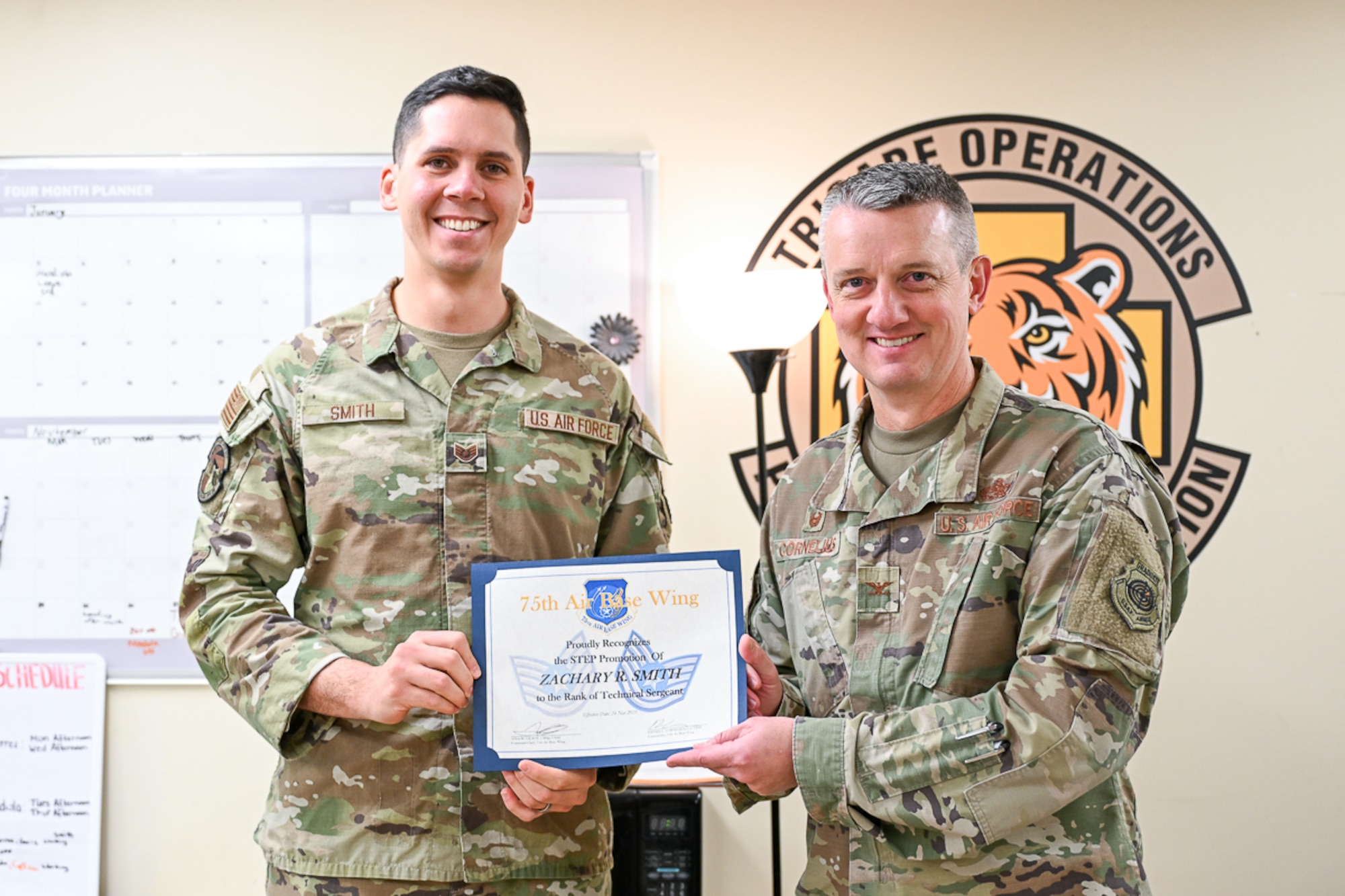 Tech. Sgt. Zachary R. Smith and Col. Daniel Cornelius hold a promotion certificate and face the camera during a Stripes for Exceptional Performers ceremony.