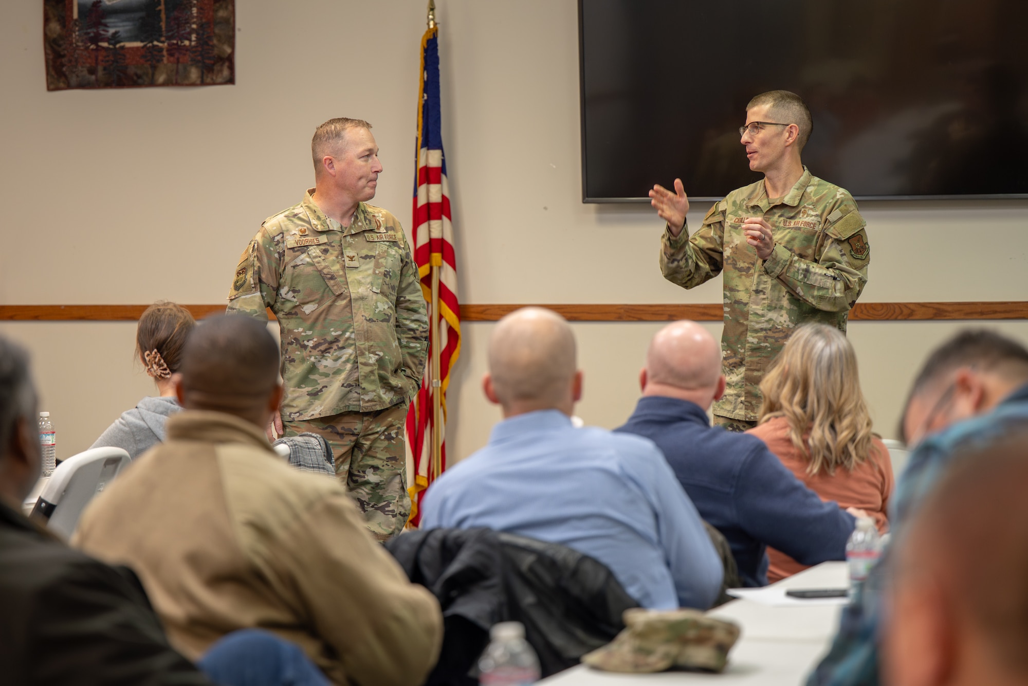 Two uniformed personnel speak to a group of people.