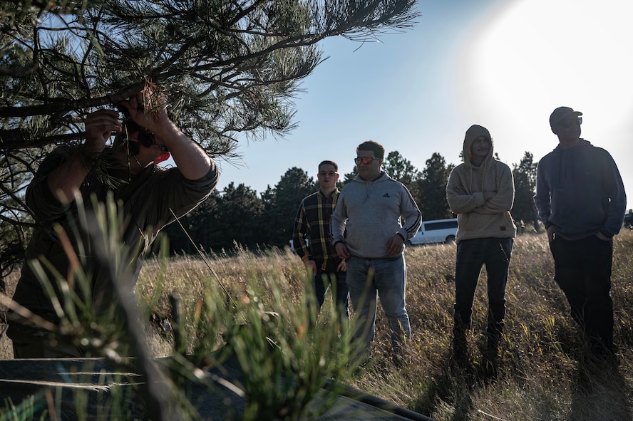 Tech. Sgt. Brett Darby, 5th Operational Support Squadron survival, evade, resistance, escape specialist, shows airmen participating in the combat survival training how to properly build shelter at Garrison, North Dakota, Oct. 9, 2025. SERE specialists are responsible for equipping Air Force aircrew with the necessary abilities to live in the wild and in hostile territory in the event that pilots are forced to land. (U.S. Air Force photo by Senior Airman Alyssa Bankston)