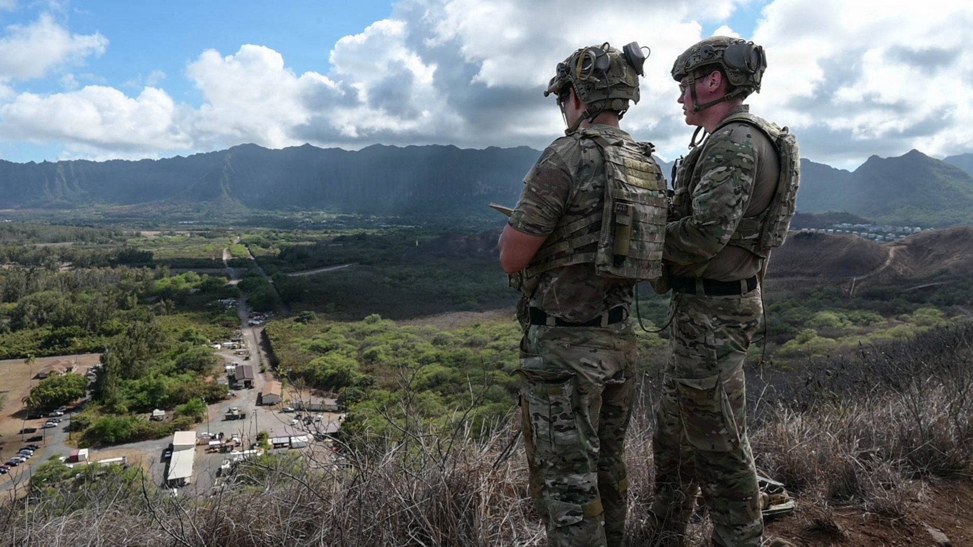 Two Airmen stand on a peak, participating in simulated airstrike training.
