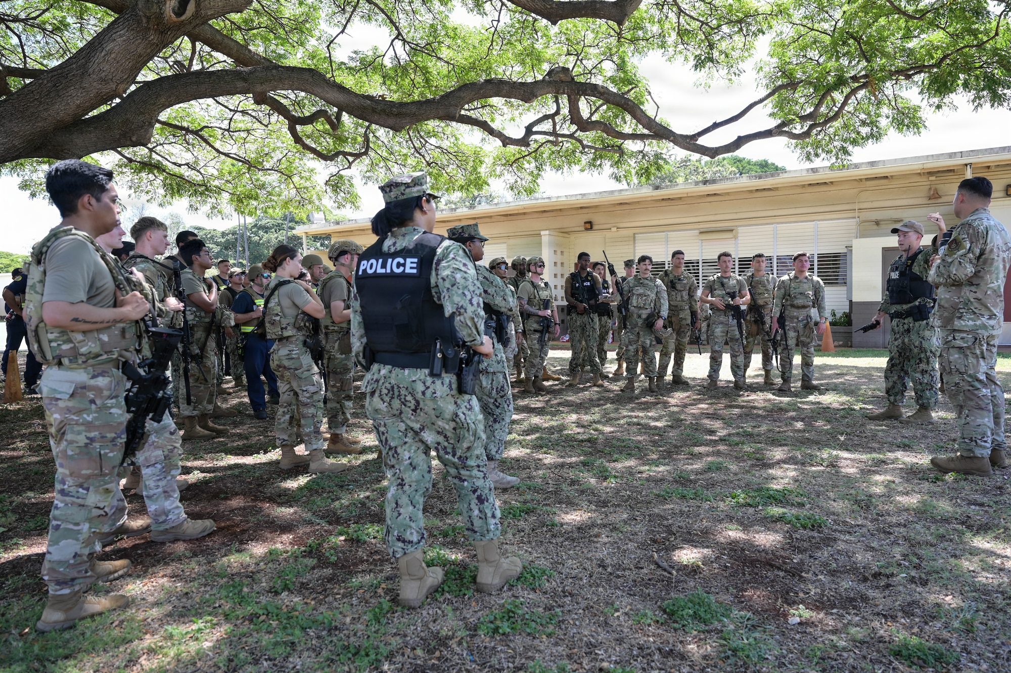 Airmen, sailors, and firefighters stand in a group while listening to instruction for an exercise.