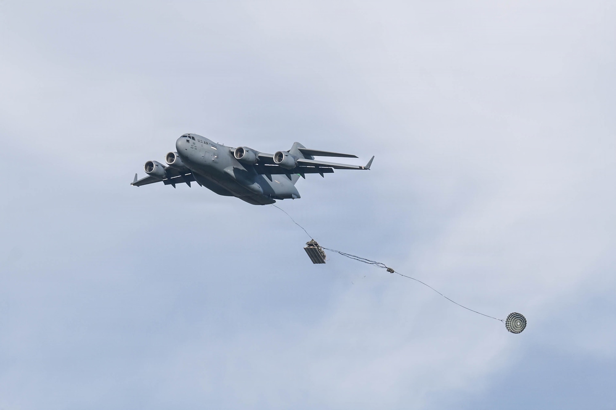 A C-17 aircraft delivers cargo in a drop zone.
